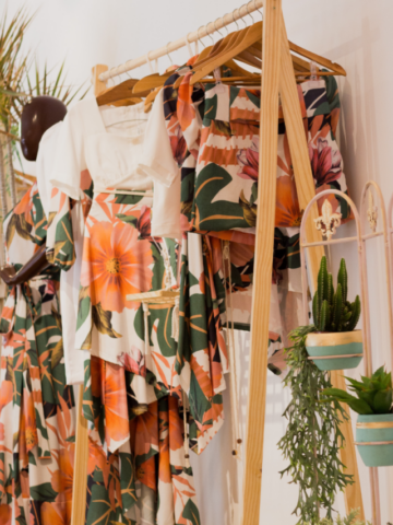 a brown wood closet with clothing handing up with a plant stand next to it.
