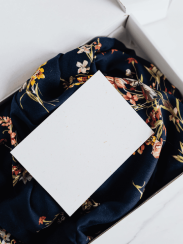 a blue floral clothing item inside a white box with a white piece of paper on top of the garment.