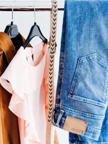 clothes rack with a brown jacket, pink shirt, cream belt, and a pair of blue jeans.