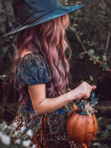 girl in a halloween costume with witch hat holding a pumpkin.