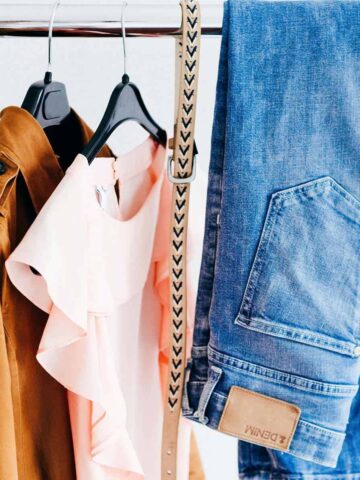 clothes rack with a brown jacket, pink shirt, cream belt, and a pair of blue jeans.