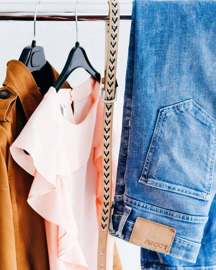 clothes rack with a brown jacket, pink shirt, cream belt, and a pair of blue jeans.
