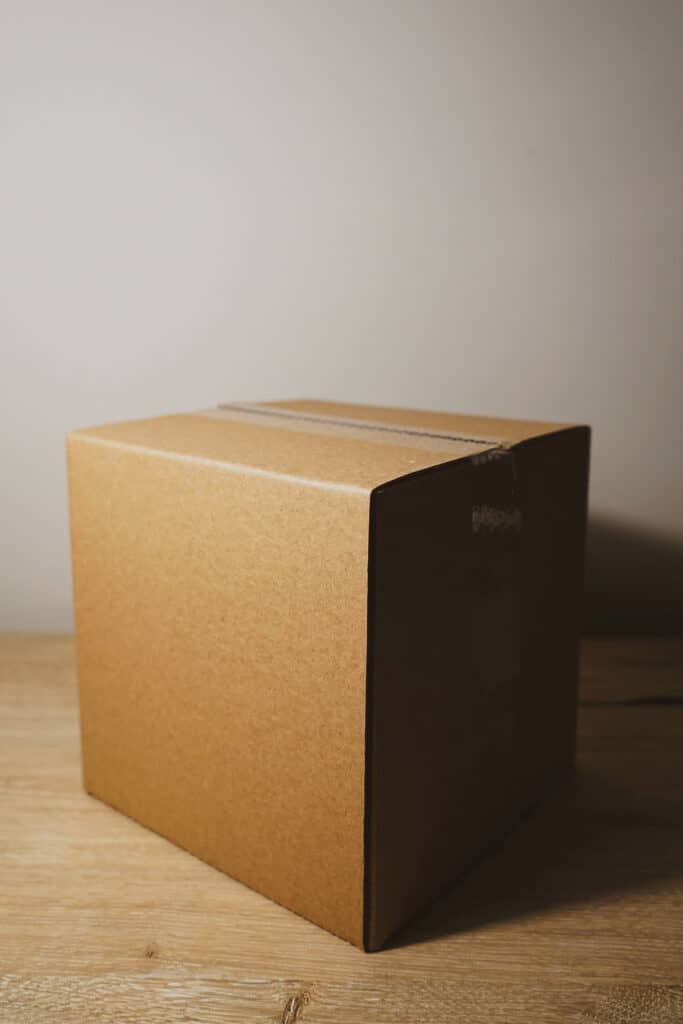 large brown cardboard box on a wood floor with a plain background.