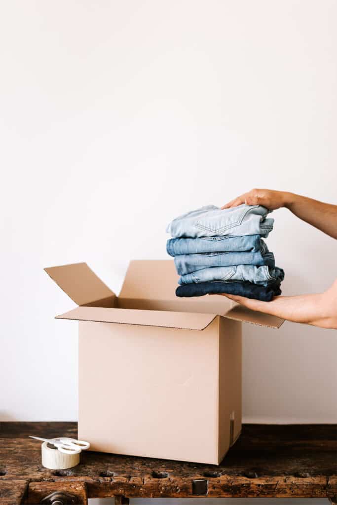 person putting 5 pairs of jeans into a brown cardboard box