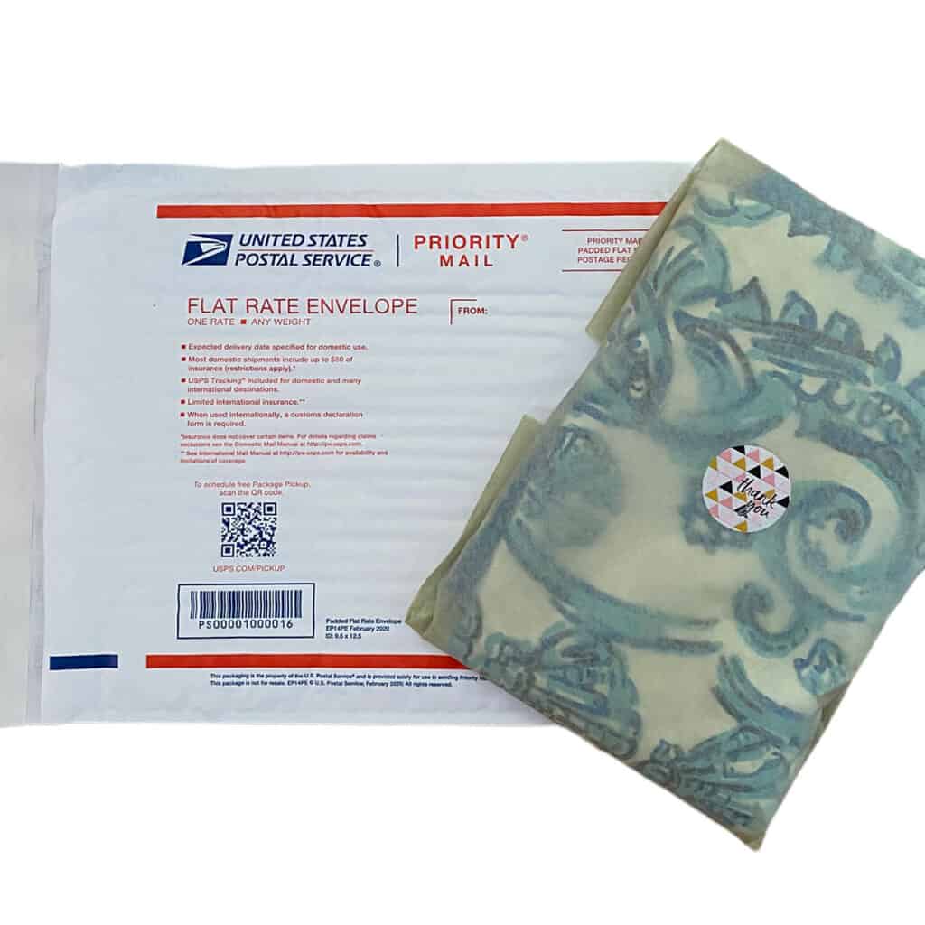 a bubble shipping mailer placed below a a dress wrapped in tissue paper with a thank you sticker on it.