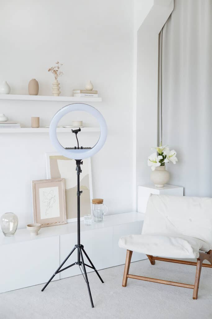 minimalist room with ring light, shelves, vases, pictures, and a chair.