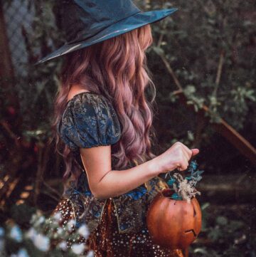 girl in a halloween costume with witch hat holding a pumpkin.