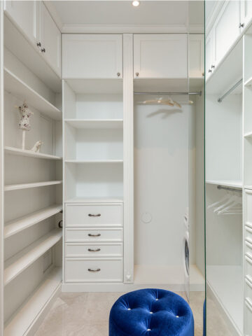 an empty closet with white shelves and a blue ottoman on the floor.