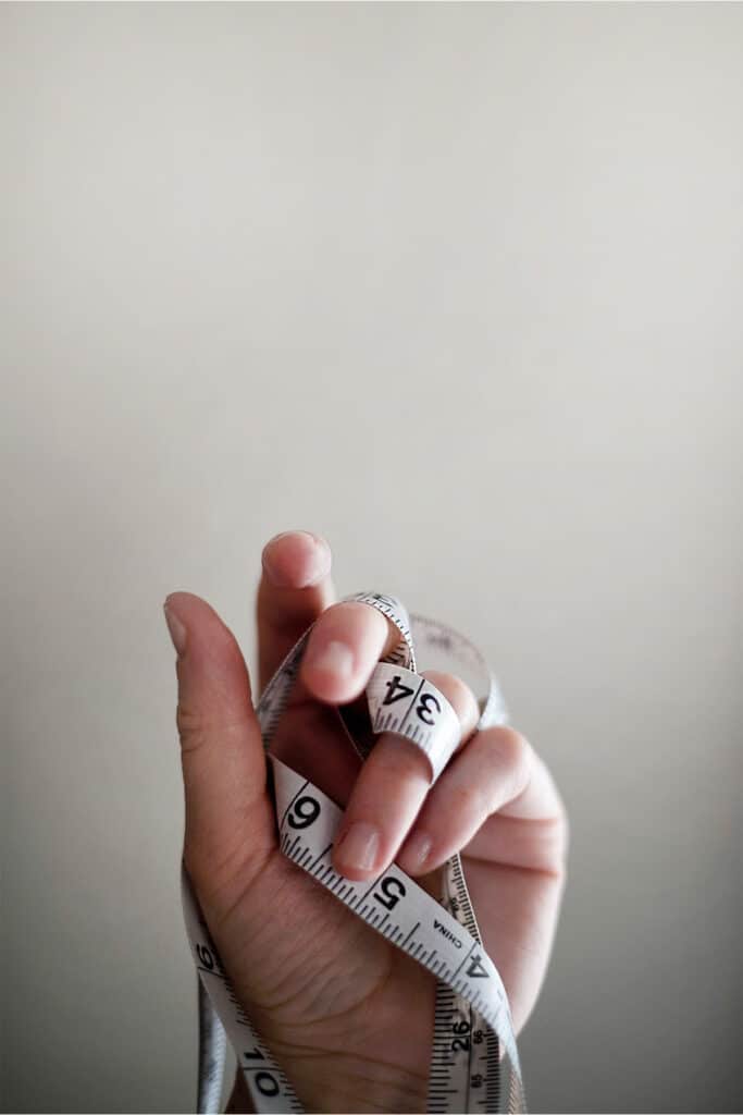 a hand holding a white tape measure with black print wrapped around the persons fingers.