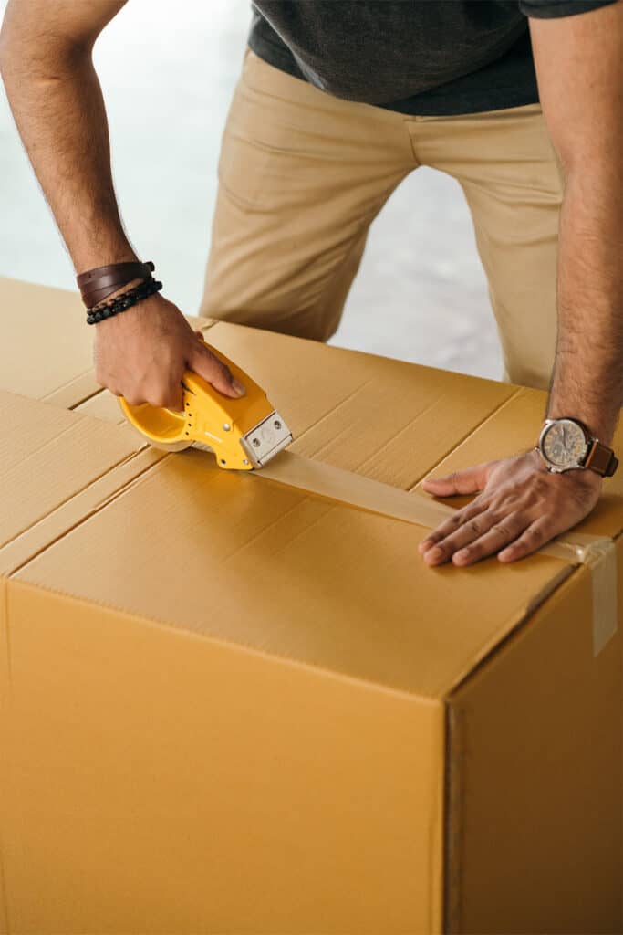 a man sealing a brown box with tape.
