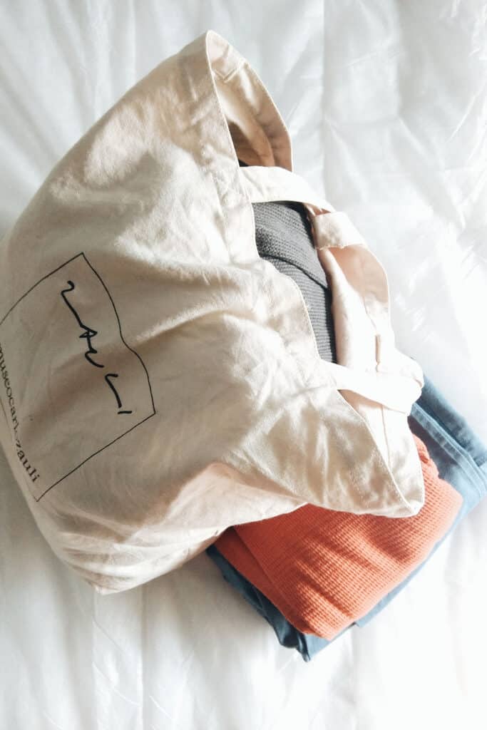 a canvas bag with clothes sitting on top of a pair of jeans and orange sweater.