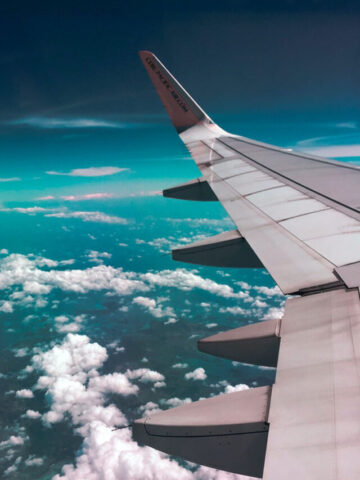 one wing of a plane with clouds in the background.