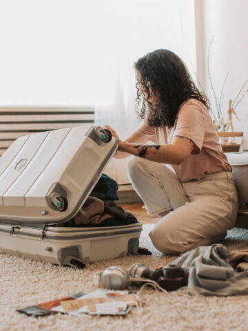 a woman sitting on the ground packing a suitcase with clothing.