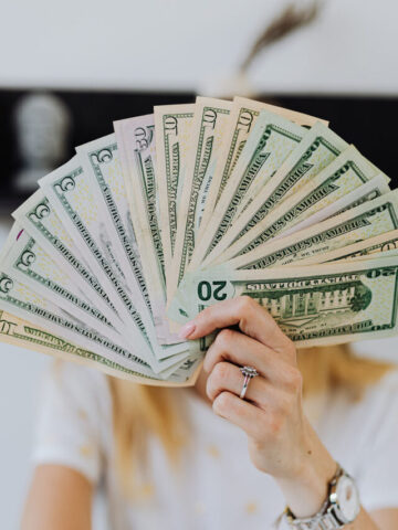 woman with a handful of fanned out cash hiding her face.