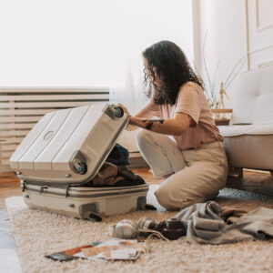 a woman sitting on the ground packing a suitcase with clothing.