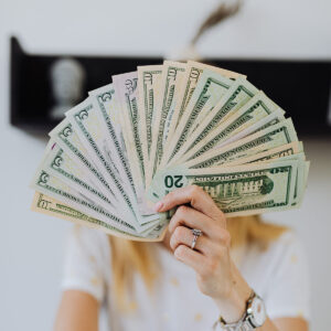 woman with a handful of fanned out cash hiding her face.