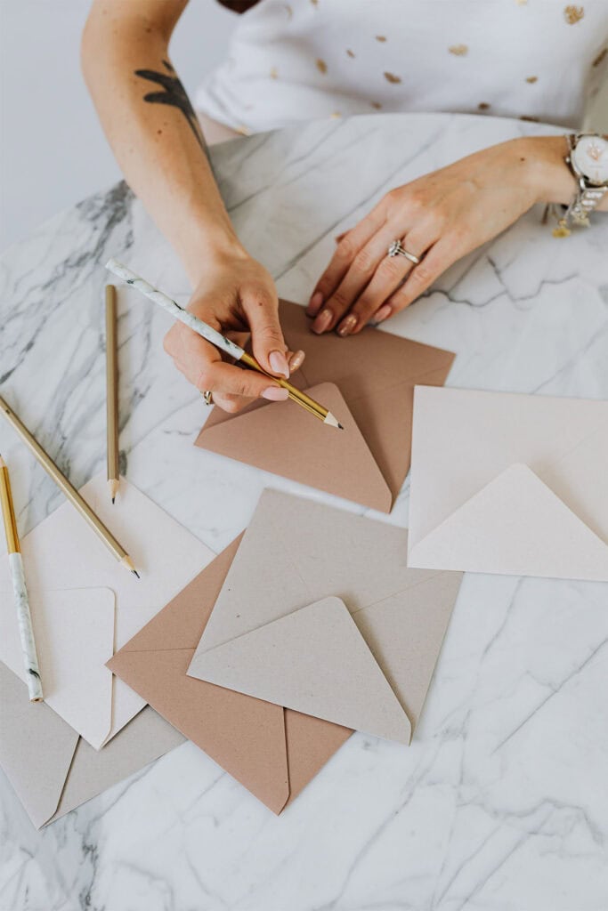 woman writing on a blank envelope with a pencil.