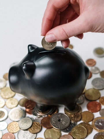 a black piggy bank with a hand putting coins into it.