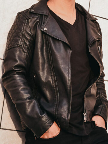 man standing against a tile wall wearing a black leather jacket.