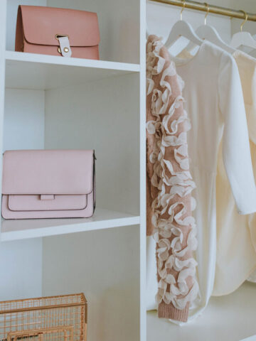 a white wooden closet with 2 purses and 4 shirts hanging up.