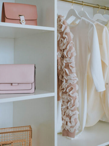 a white wooden closet with 2 purses and 4 shirts hanging up.