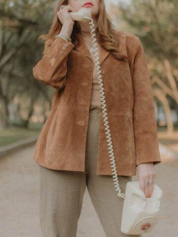 woman holding a dial up phone wearing a brown suede jacket.