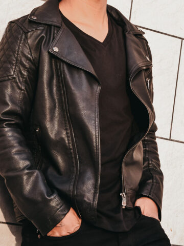 man standing against a tile wall wearing a black leather jacket.