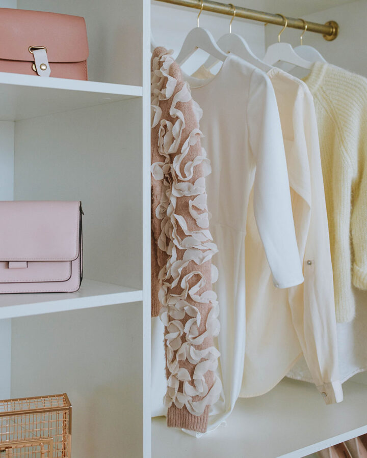a white wooden closet with 2 purses and 4 shirts hanging up.