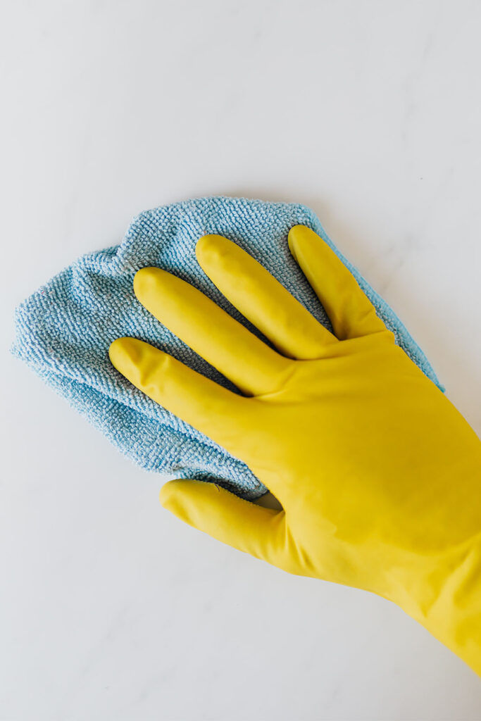 person wearing a yellow glove wiping down a white table with a blue microfiber cloth.