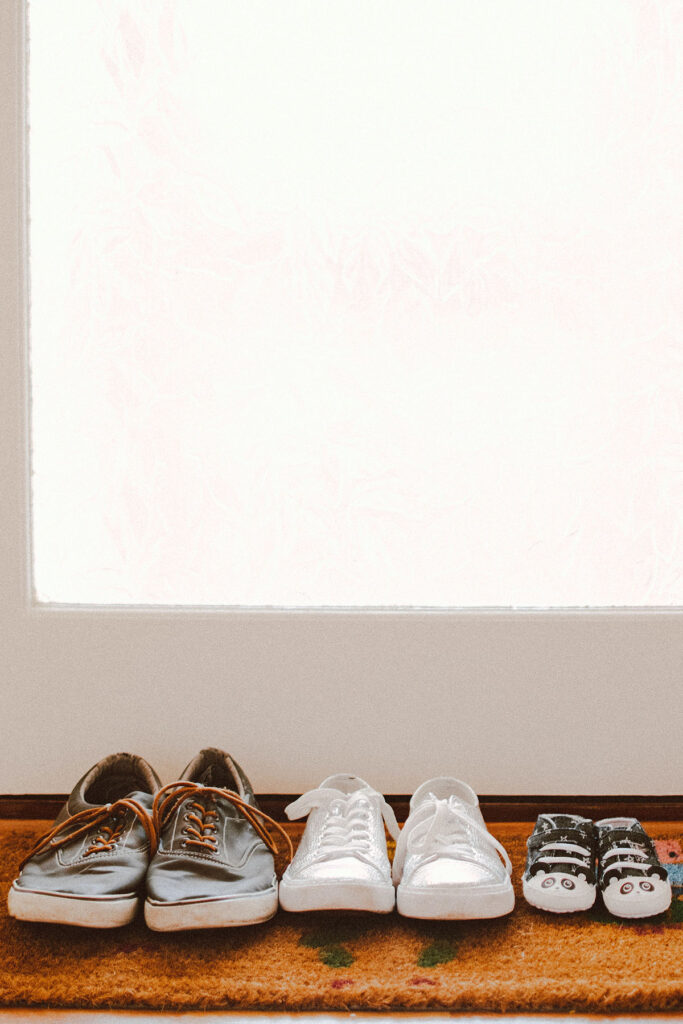 three pairs of shoes on a brown mat in front of a door.