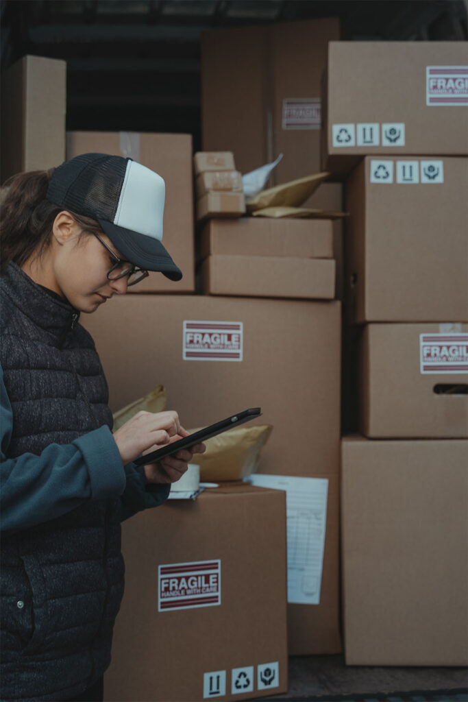woman on a tablet standing in front of brown cardboard boxes.