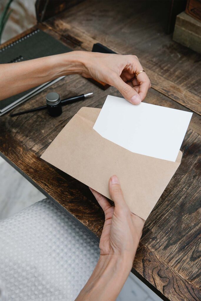 a womans hands putting a white piece of paper into a brown envelope.