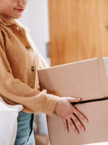 a girl carrying two cardboard boxes and a nude canvas bag.