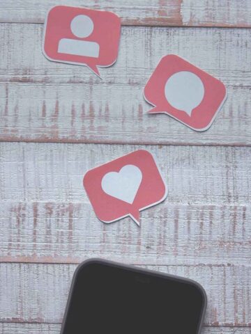 a phone on a white wood table with a heart, speech bubble, and person icon above the phone.