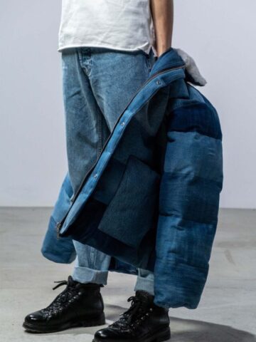 a man wearing black shoes, jeans, a white shirt, and holding a blue puffer coat.