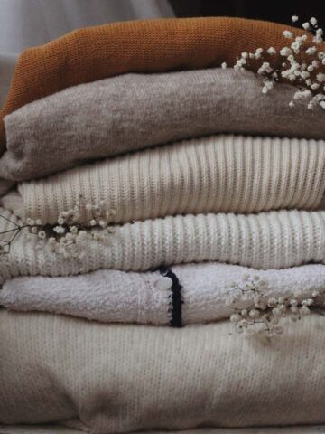 a pile of folded sweaters on top of one another with babys breath stems dispersed throughout.