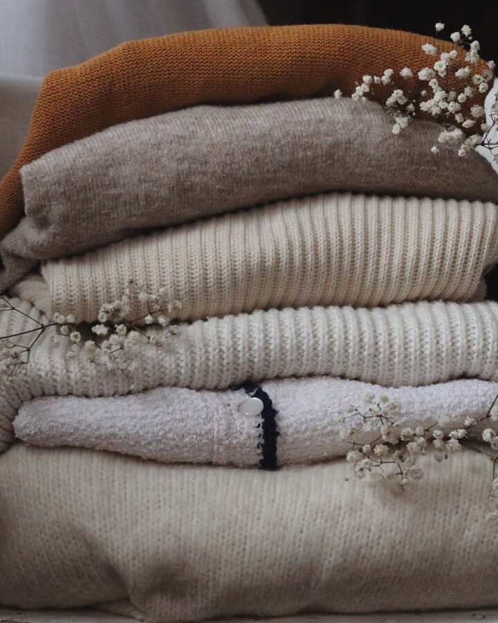 a pile of folded sweaters on top of one another with babys breath stems dispersed throughout.
