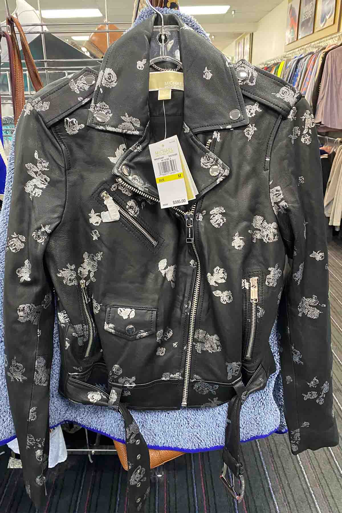 a black floral michael kors jacket hanging on a clear plastic hanger.