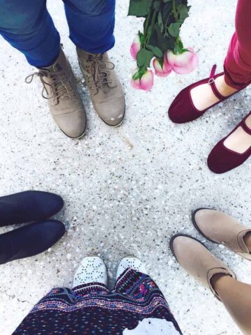 five women standing in a circle with a downward angle showing the ground and their shoes.