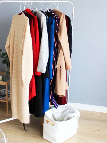 a white clothes rack with coats and sweaters hanging on it.