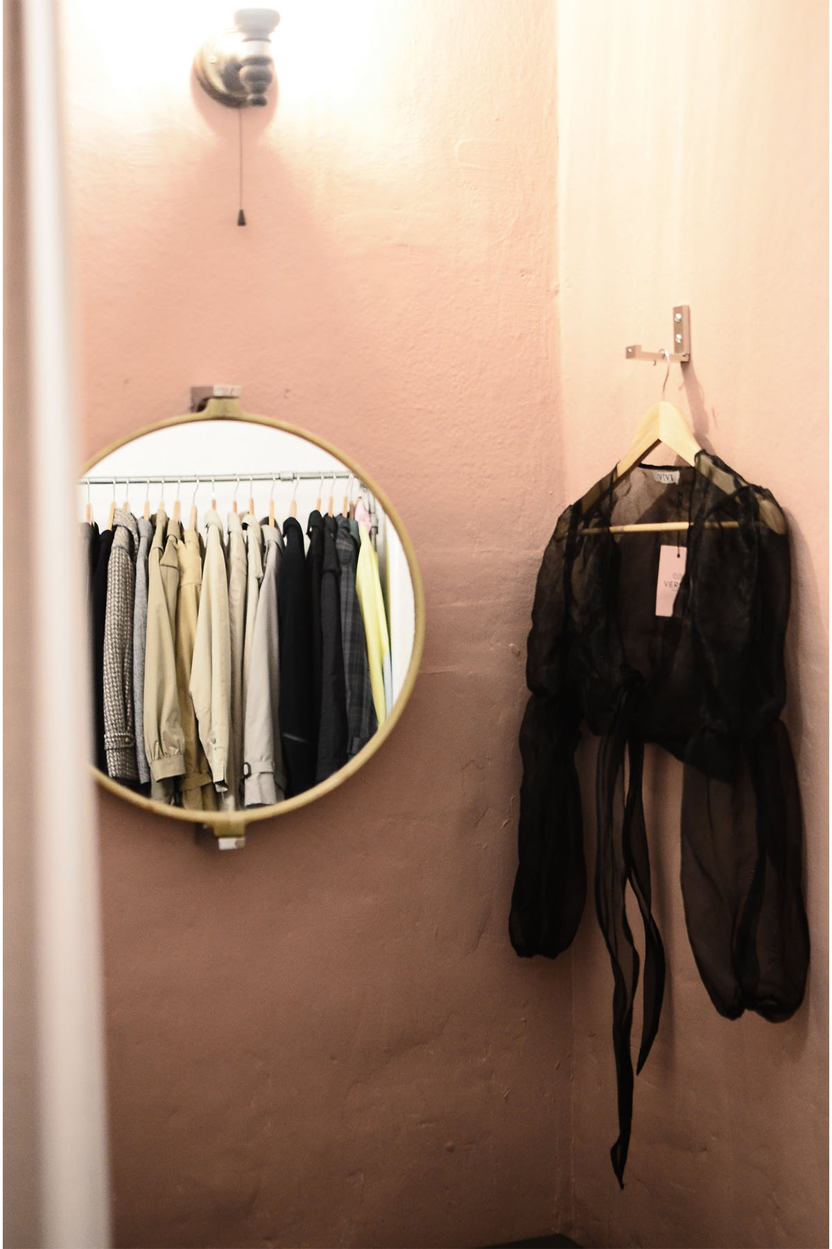 a dressing room with a mirror and a black long sleeve shirt hanging on a hook.